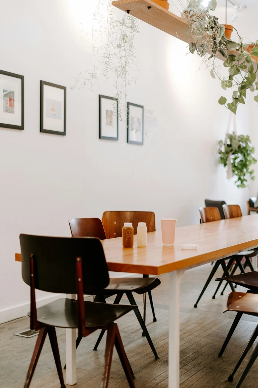 Salle de réunion avec table en bois, chaise moderne, mur blanc et plante verte tombante